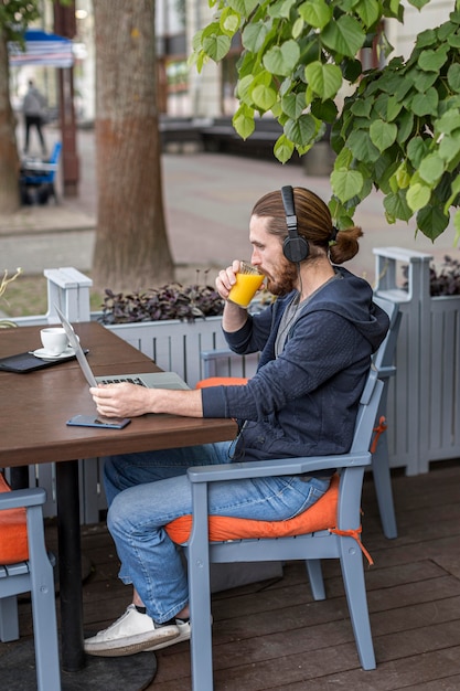 Free photo man enjoying juice at a city terrace while working on laptop