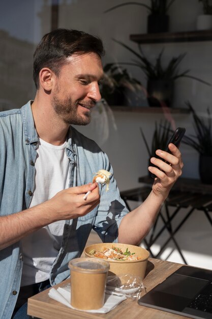Человек, наслаждающийся едой на вынос и с помощью смартфона
