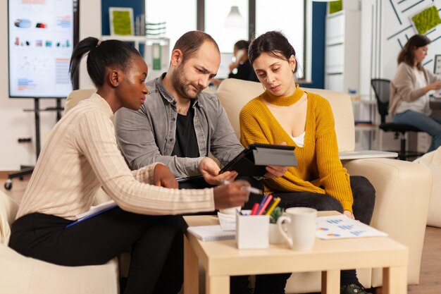 Man executive instructing diverse employees in new modern company office room before business meeting with partners analysing reports on tablet