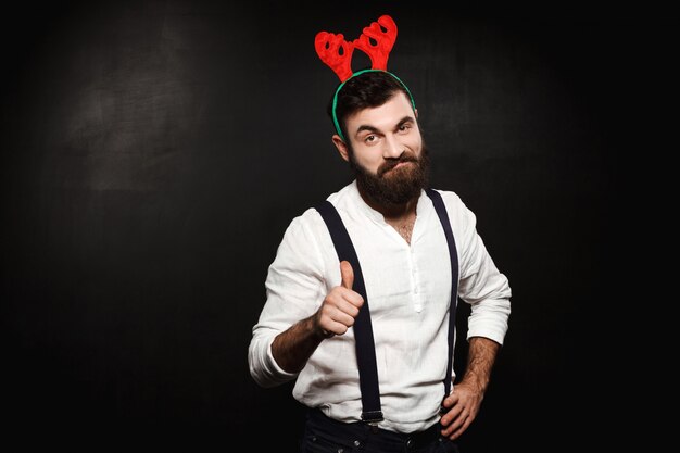 Man in fake deer horns showing okay over black.