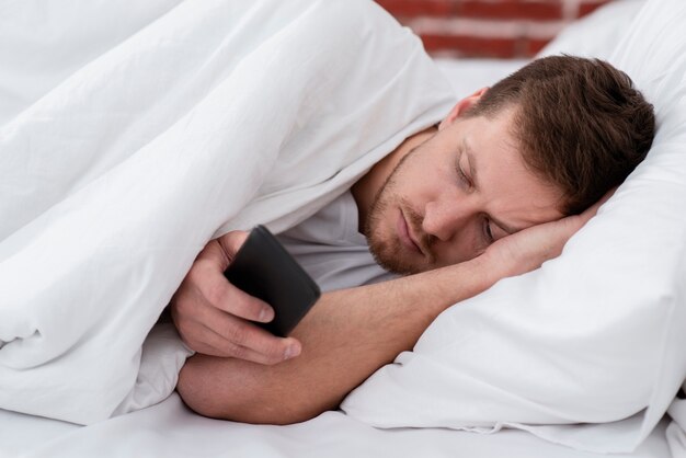 彼の携帯電話を押しながら眠りに落ちる男
