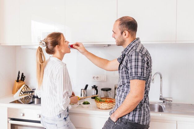 Man feeding fresh healthy red radish to his girlfriend in the kitchen