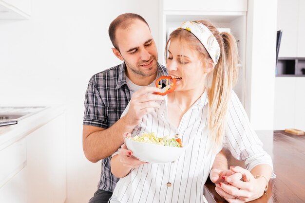 Man feeding salad to his wife in the kitchen
