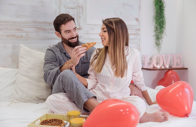 Foto gratuita equipaggi la donna d'alimentazione con il croissant sul letto