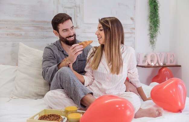 Man feeding woman with croissant on bed 