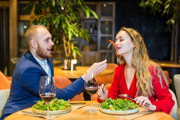 Мужчина кормит женщину с салатом в ресторане