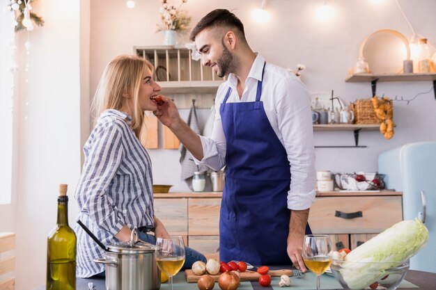 Мужчина кормит женщину с помидорами на кухне