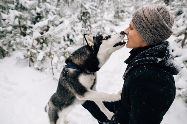 冬の雪の天気で屋外で口から口に彼のハスキー犬のビスケットを人が給餌する