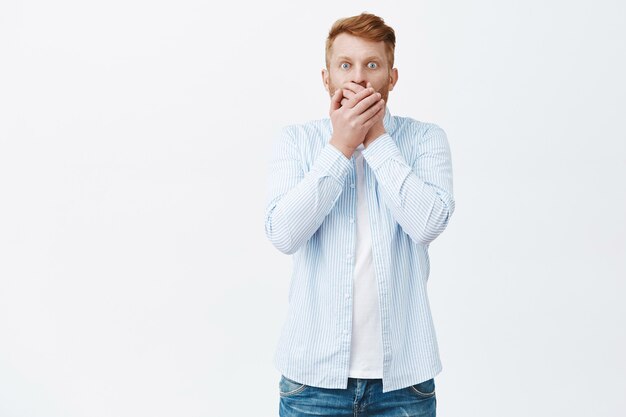 Man feeling regret saying secret. Portrait of shook and worried handsome mature man with ginger hair, covering mouth from shock and amazement being astonished, popping eyes