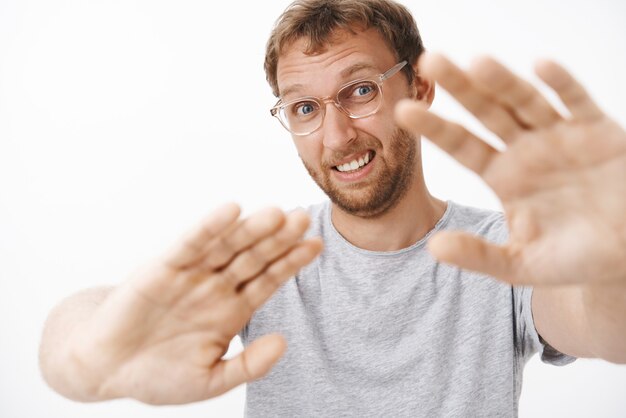 Man feeling shy hates being photographed pulling hands towards to cover face from flashlight making confused awkward face raising eyebrows and squinting feeling uncomfortable
