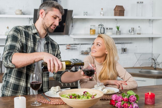 Man filling glass by wine from bottle near woman in kitchen 