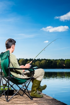 Человек, ловящий рыбу на озере, сидя на пристани рядом с водой