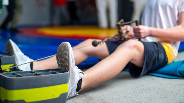 A man on the floor of the gym doing an exercise with a simulator