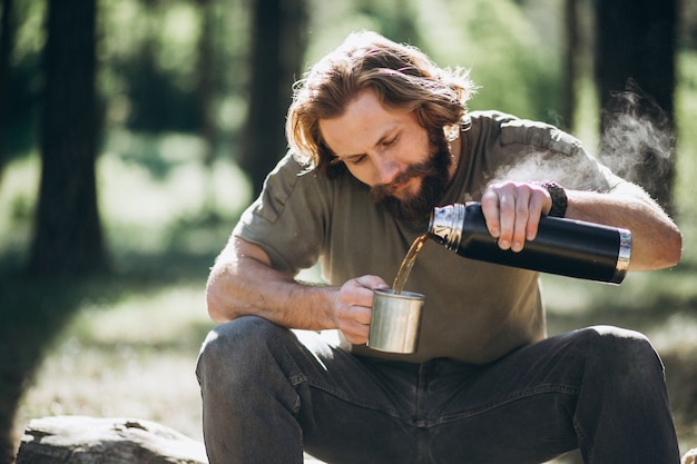 Man in forest with tea by fire