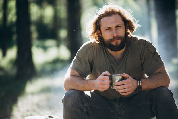 Man in forest with tea by fire