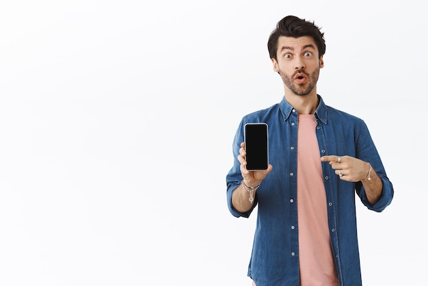 Free photo man found excellent online shop to buy gifts pointing smartphone and telling it must have excited happy handsome bearded guy showing something on mobile screen with pleased expression