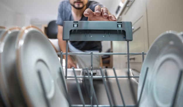 A man in front of an open dishwasher takes out clean dishes after washing.