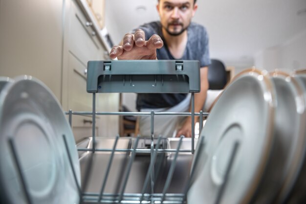 A man in front of an open dishwasher takes out clean dishes after washing