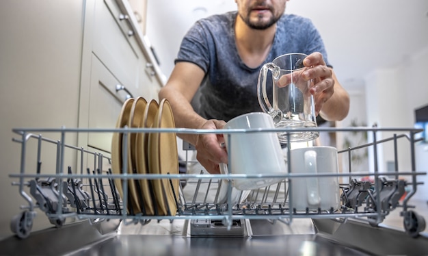 開いた食器洗い機の前にいる男性が、皿を出し入れします。