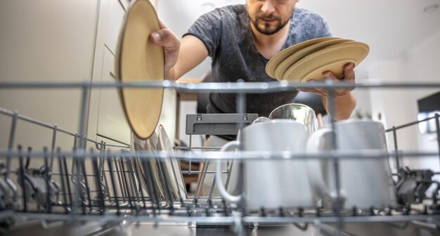 開いた食器洗い機の前にいる男性が、皿を出し入れします。