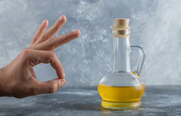 Man gesturing ok with hand behind of bottle of oil. High quality photo