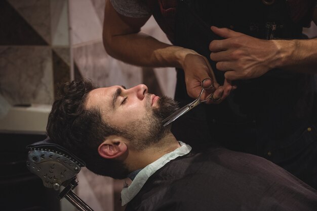 Мужчина подстригает бороду ножницами