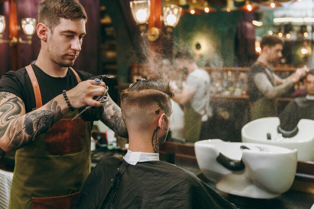 理髪店​で​流行り​の​散髪​を​している​男性​。​クライアント​に​サービス​を​提供する​入れ墨​の​男性​の​ヘア​スタイリスト​。