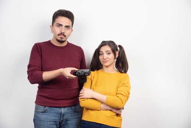 Man giving a camera to young woman on a white wall.