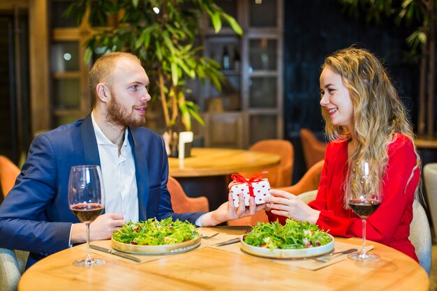 Man giving gift box to blond woman at table 