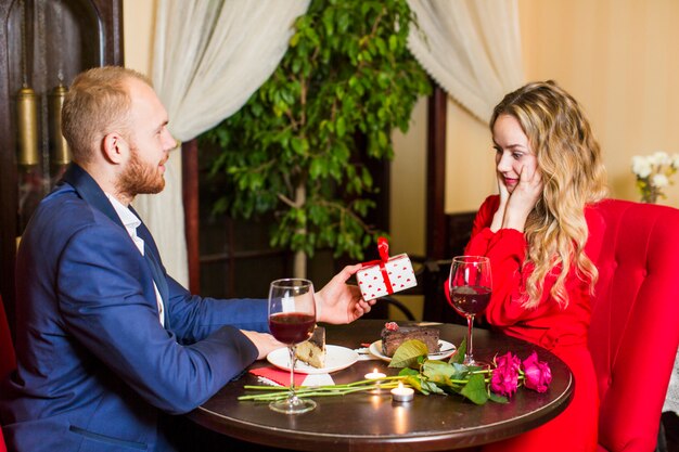 Man giving gift box to woman at table in restaurant 