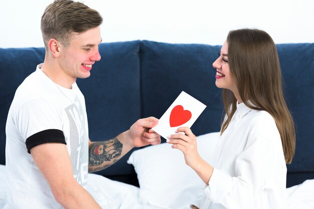 Man giving greeting card to woman in bed 