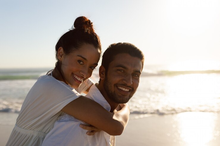 Free Photo man giving piggyback ride to woman on the beach