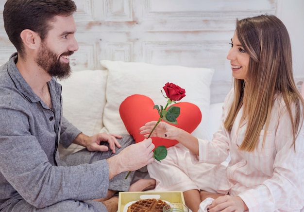 Man giving red rose to woman on bed