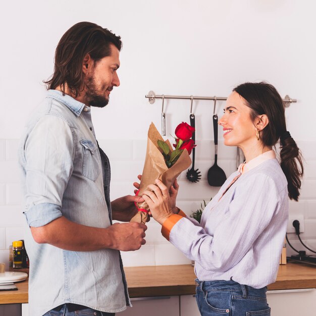 Man giving red roses bouquet to woman in kitchen