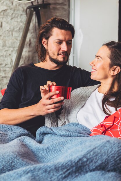 Man giving small gift box to woman on couch