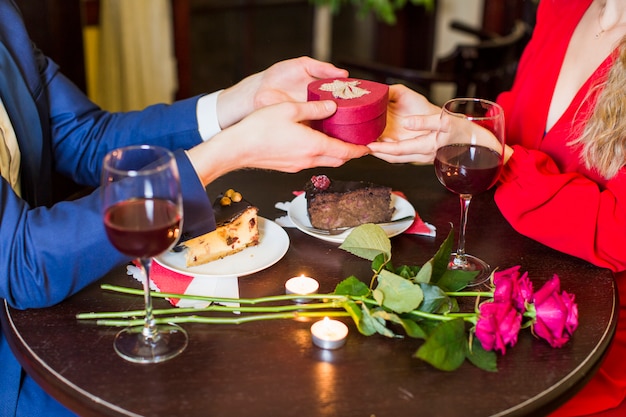 Free photo man giving small gift box to woman at table in restaurant