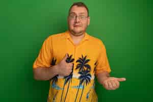 Free photo man in glasses and hawaiian shirt  confused showing thumbs up standing over green wall