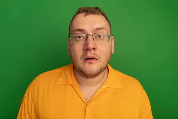 Man in glasses and orange shirt  confused and very anxious standing over green wall