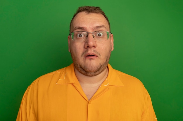 Man in glasses and orange shirt  surprised and worried standing over green wall