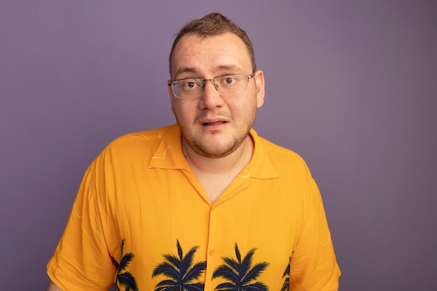 Man in glasses wearing orange shirt  happy and positive smiling standing over purple wall