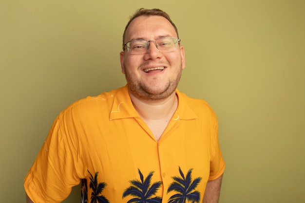 Free photo man in glasses wearing orange shirthapy and cheerful  with big smile on face standing over green wall