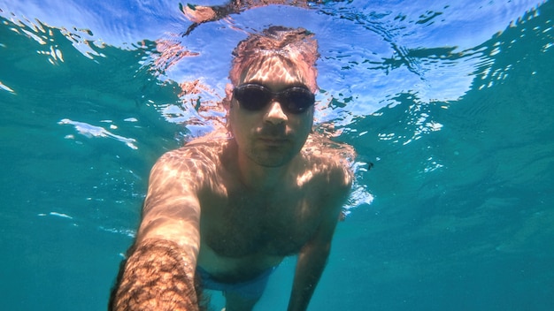 Man in goggles swimming under the blue and transparent water of the Mediterranean sea. Holding the camera