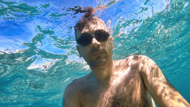 Man in goggles swimming under the blue and transparent water of the Mediterranean sea. Holding the camera