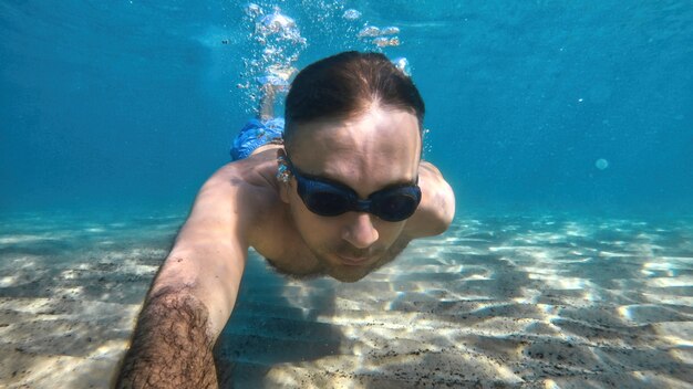 地中海の青く透明な水の下で泳ぐゴーグルの男。カメラを持って