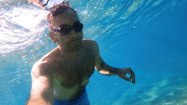 Man in goggles swimming under the blue and transparent water of the Mediterranean sea. Holding the camera