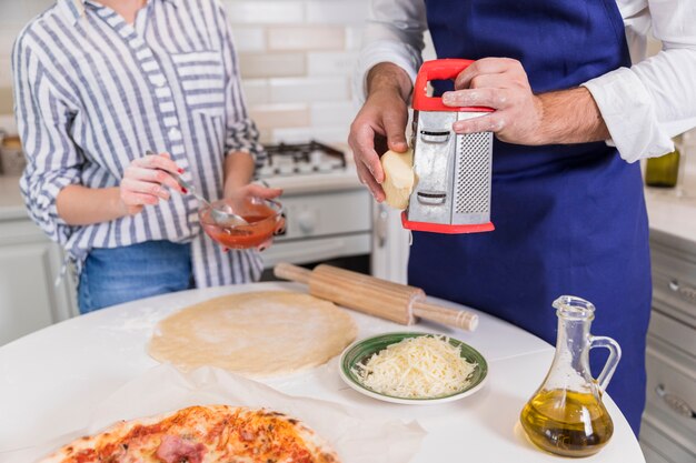 Man grating cheese for pizza with woman in kitchen