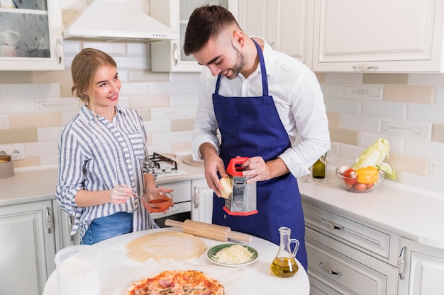 Man grating cheese for pizza with woman 