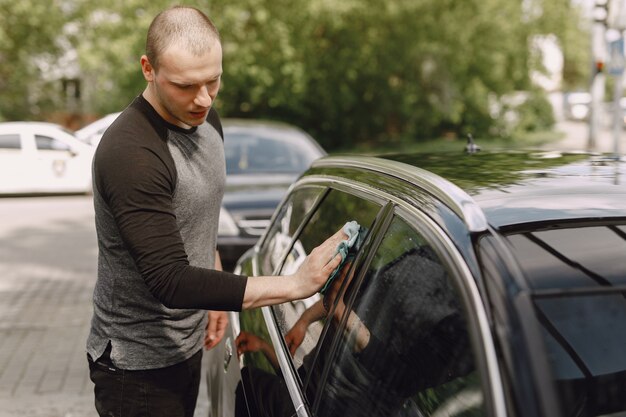 Man in a gray sweater wipes a car in a car wash