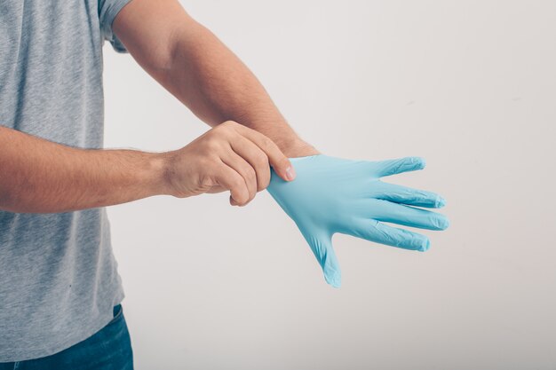 A man in gray t-shirt wearing medical gloves in white background .  