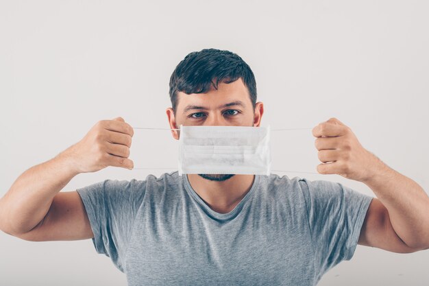 A man in gray t-shirt wearing medical mask in white background .  